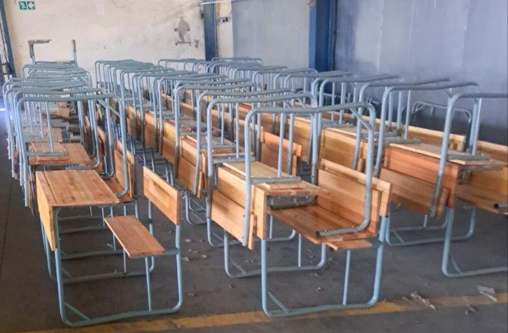 Rows of finished wooden and steel school desks in the fabrication workshop